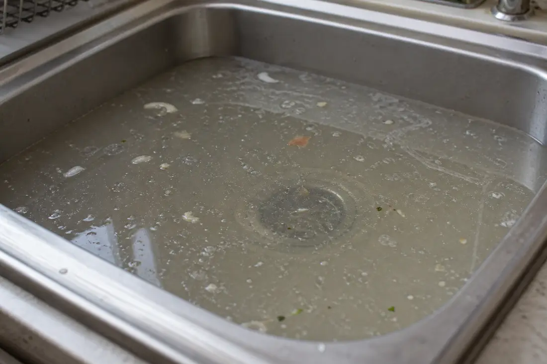 Mit stehendem, trübem Wasser gefülltes Küchenspülbecken bei einem verstopften Abfluss